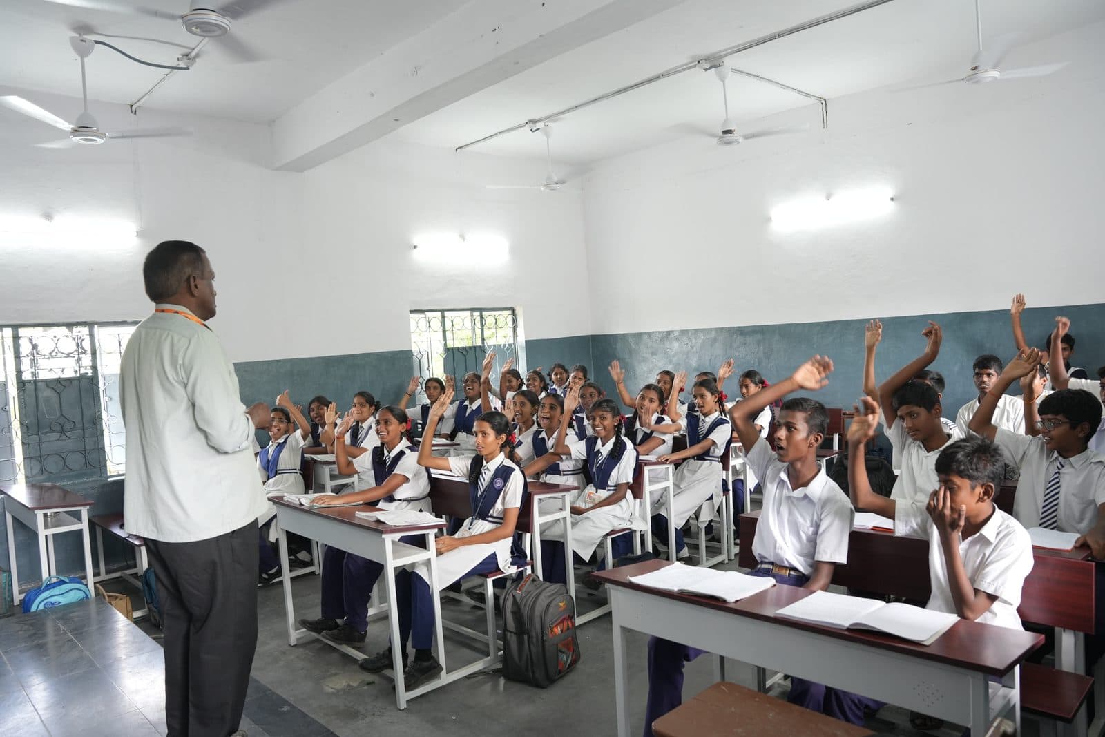 A senior class with students raising their hands while the teacher stands at the front