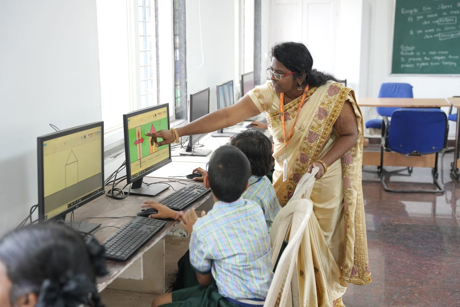 A teacher leaning in to guide a student working at a computer