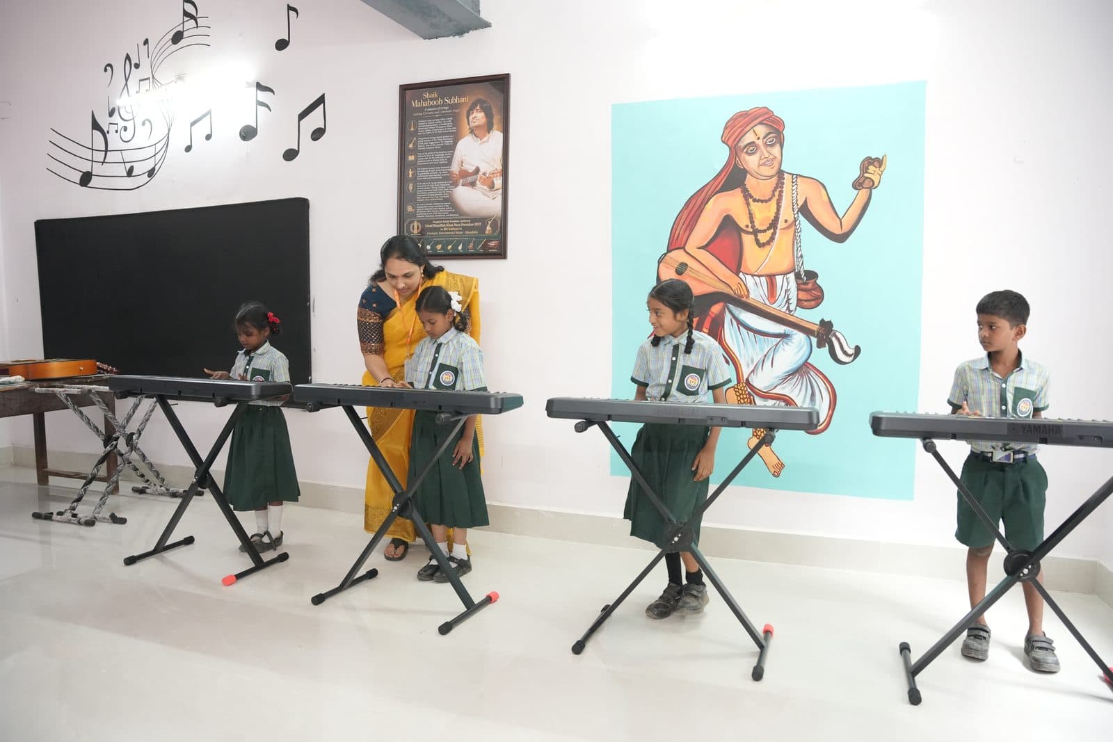 Young students standing at electronic keyboards during a music lesson, with a mural of Saraswati behind them