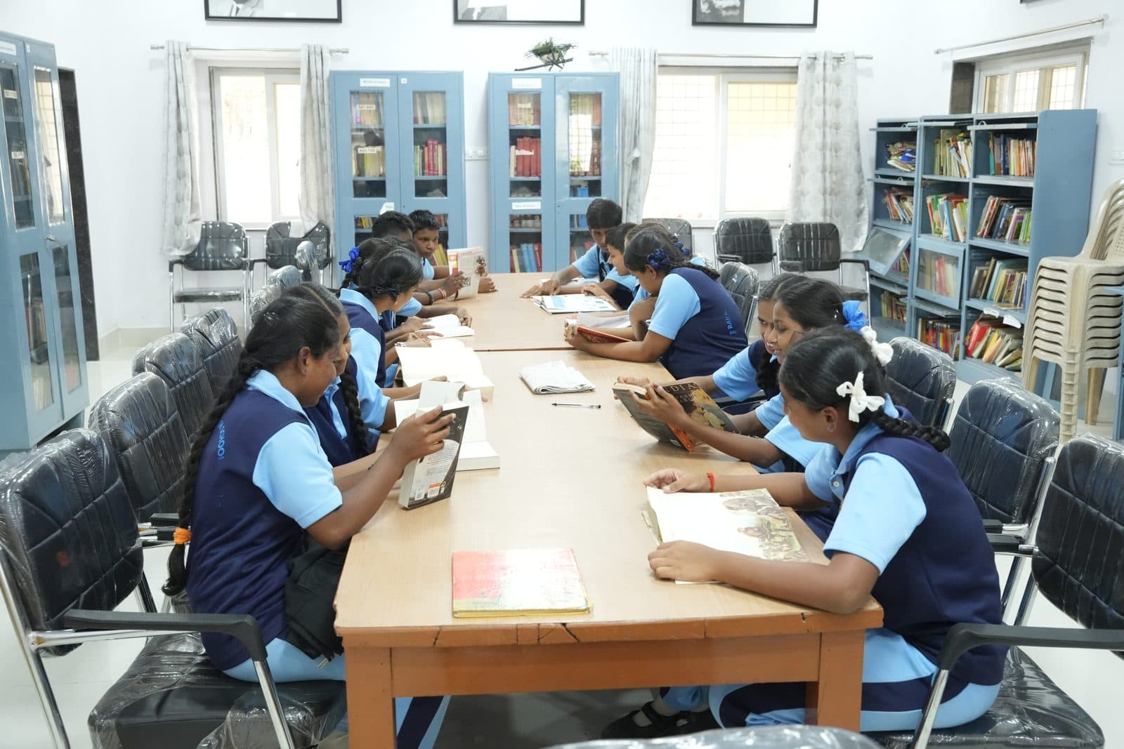 Students reading books together at the library table, surrounded by stocked shelves