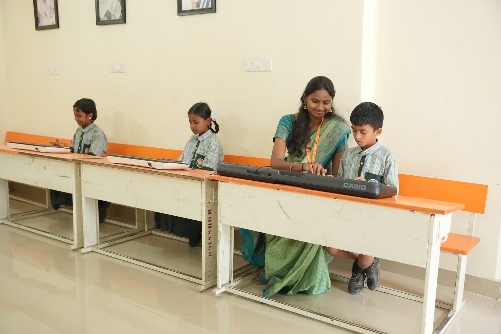 A music teacher seated beside two students, guiding their hands on a keyboard