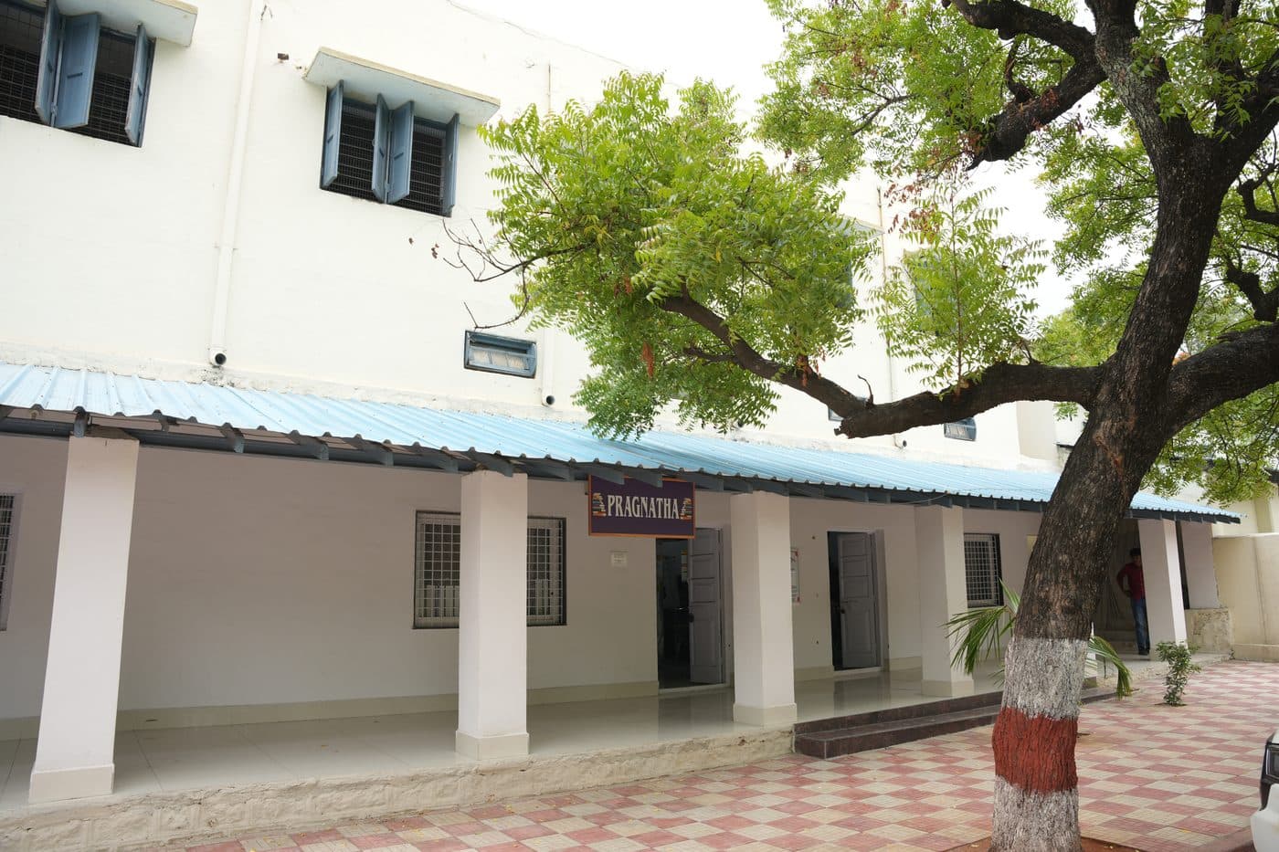 The Pragnatha block, a single-storey building with a covered verandah shaded by a large tree