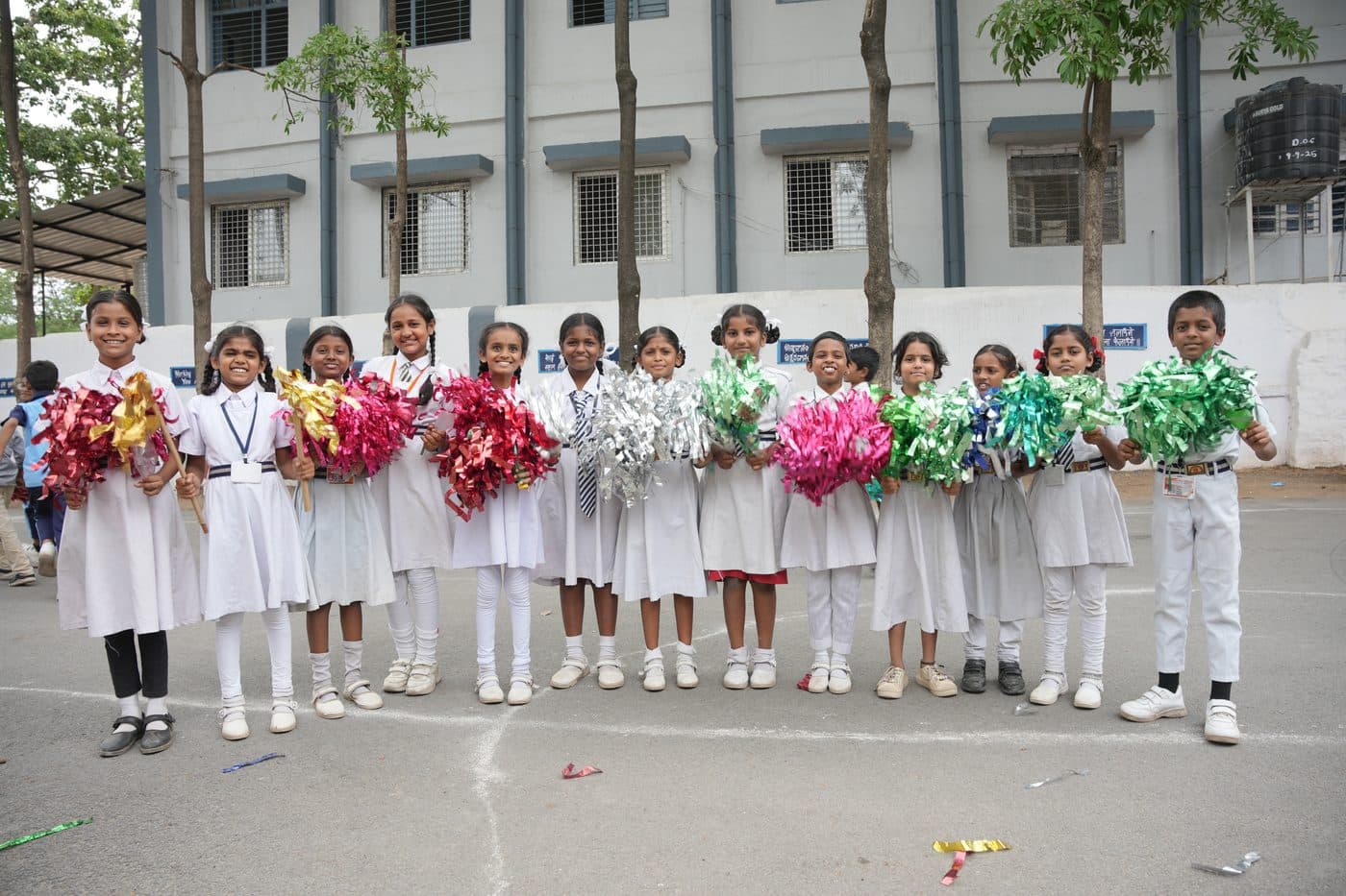 A line of students raising decorative pom-poms outside the school building