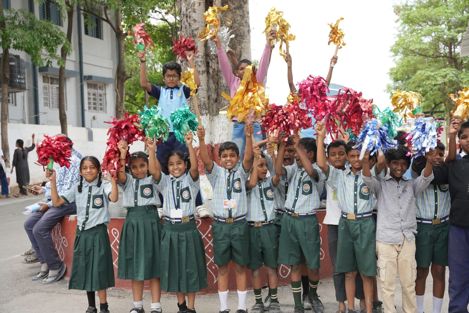 Primary students in green uniform holding up colourful pom-poms before a programme