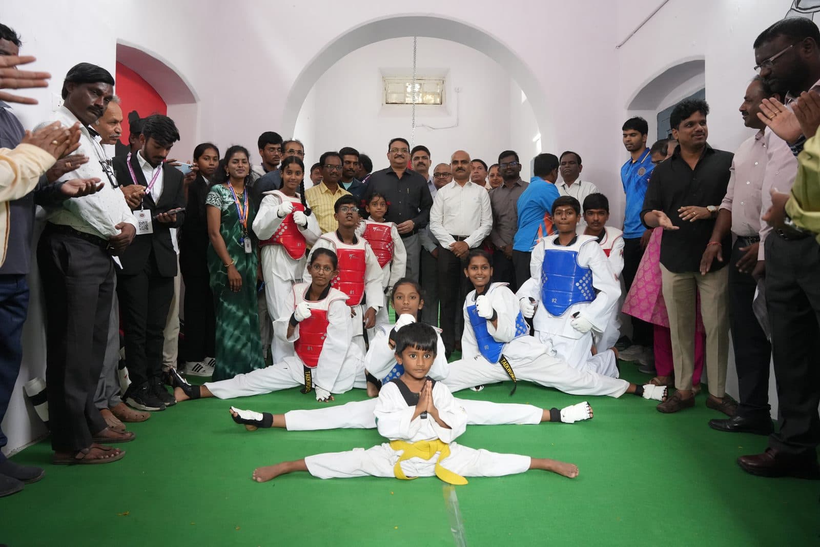 Taekwondo students in uniform and sparring gear posed together, one holding a full split at the front
